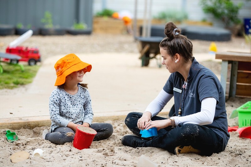 Child and carer sitting down in sandpit